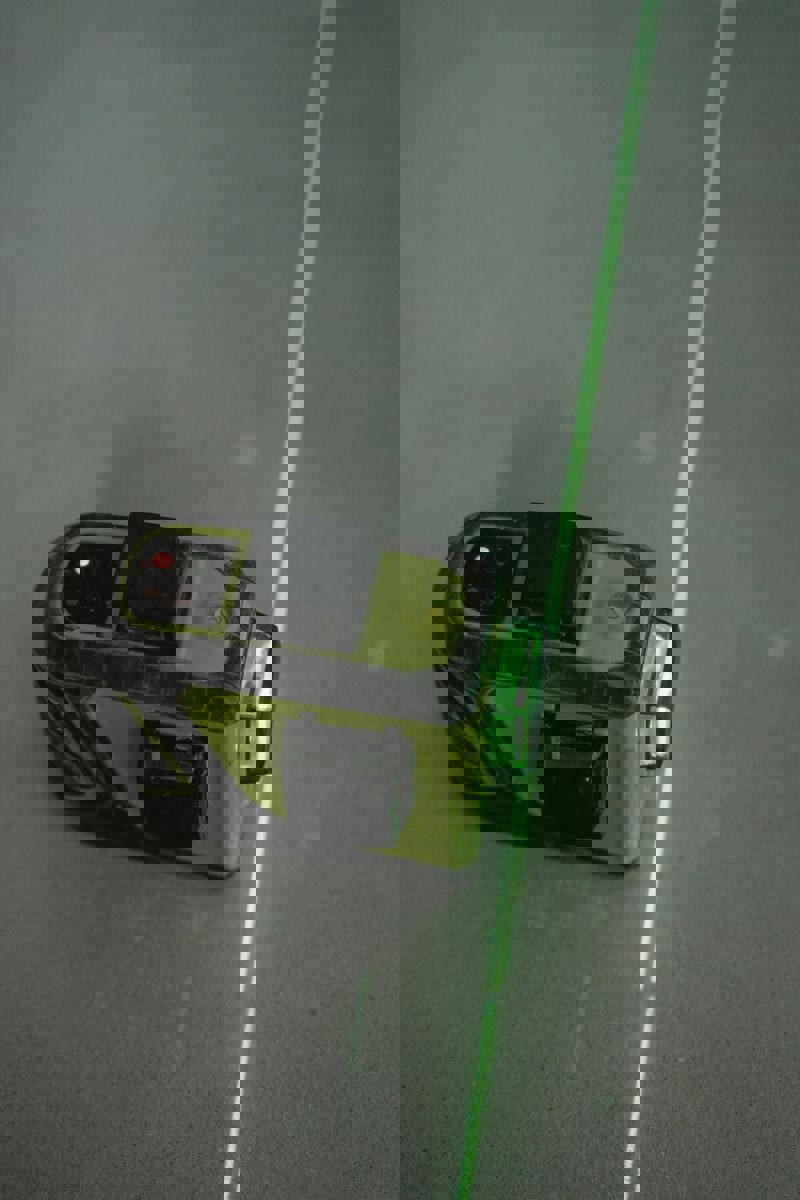 Grön laserpass på ett betonggolv som markerar en rak linje för mätning och byggarbete.