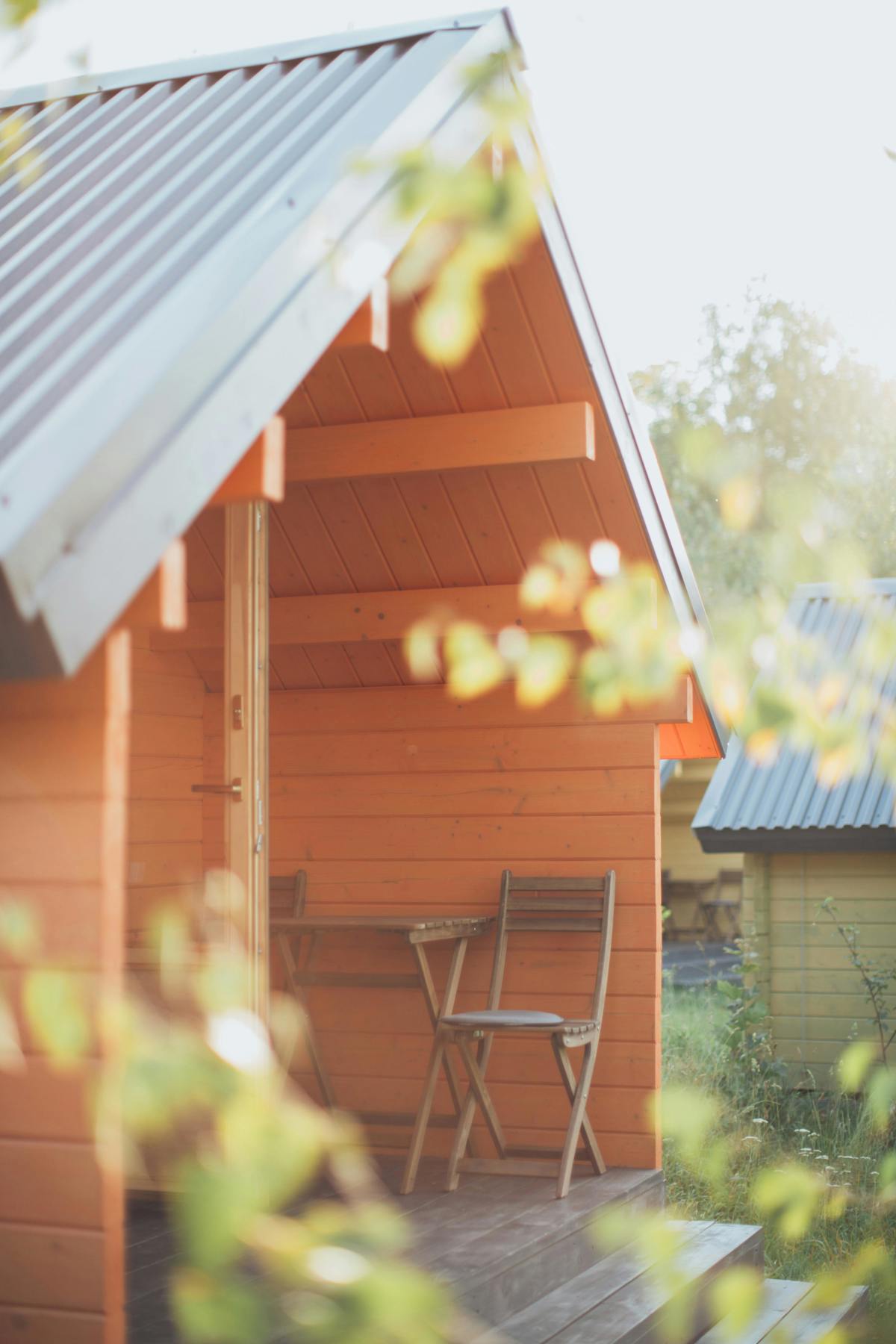Mysig liten trästuga med veranda, bord och stolar i morgonsol