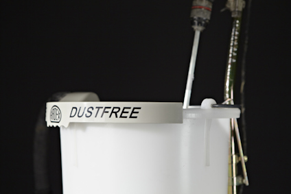 Vit hink med texten "DUSTFREE" i svart, mot en mörk bakgrund.