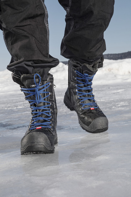 En person går på is och har på sig svarta vinterstövlar med blåa skosnören.