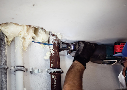 Person som använder ett elverktyg för att såga ett rör intill en vägg, omgivet av isoleringsmaterial.