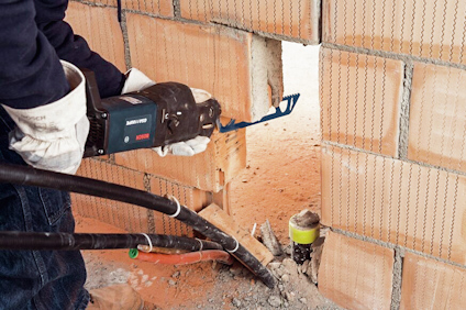 Person som sågar ett hål i tegelvägg med en elektrisk såg, iförd skyddshandskar.