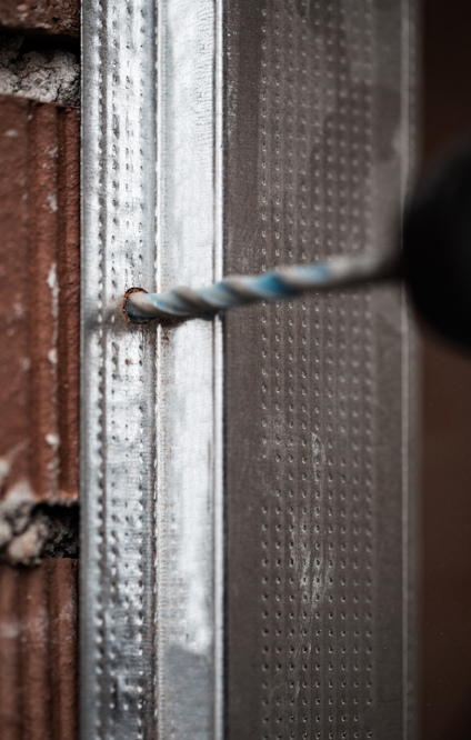 Metallprofil borras fast på tegelvägg.