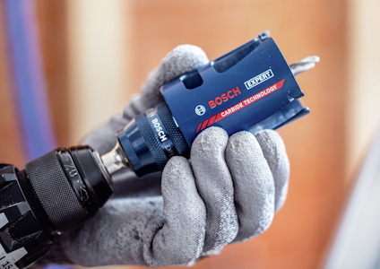 En hand i arbetshandske håller en blå Bosch Expert borr med spets av karbidteknologi.