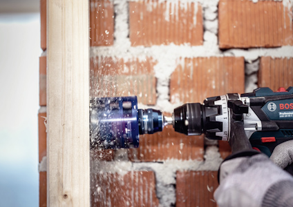 Borrmaskin med anpassat borrhuvud används för att borra ett hål genom trä mot en tegelvägg.