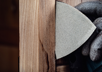 Hand i handske slipar trämöbel med sandpapper.