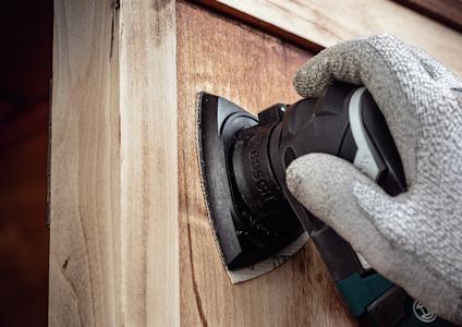 Person med handske slipar trädörr med Bosch slipmaskin.
