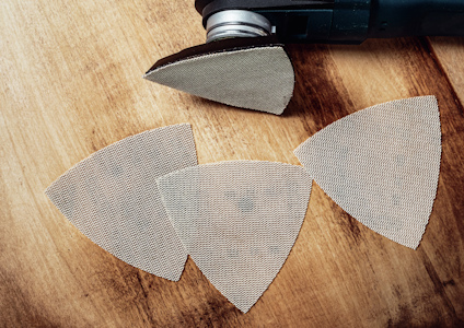 Trekantiga sandpapper av metall på ett träbord, anslutna till ett elverktyg.