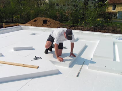 Person monterar vita isoleringspaneler på marken utomhus. Verktyg och träbit syns runt omkring.