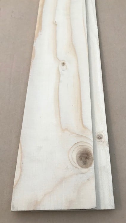Passbit av plywood med tydlig ådring och kvistar mot en beige bakgrund.