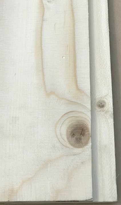 Närbild på falsen på en ljus plywoodbit med tydlig ådring och en rund kvistmärkning.