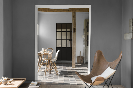 Rum med grå väggar, en brun läderstol och ett bord med stolar. Trägolv och synligt träbjälke i taket.