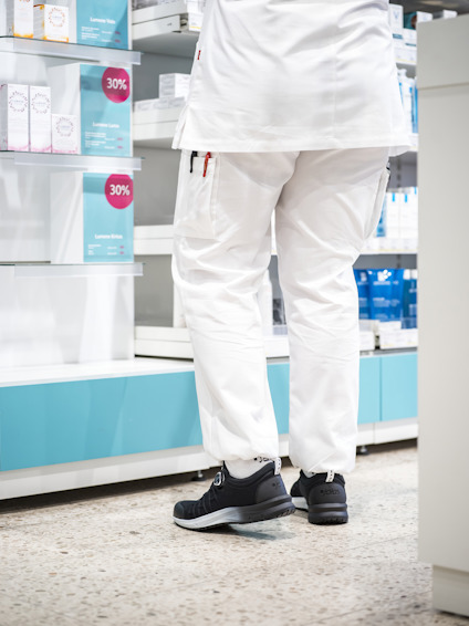 Person i vita arbetskläder och svarta skor i en butik, står framför hyllor med produkter och 30% rea-skyltar.