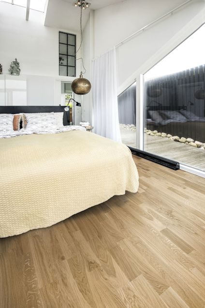 Sovrum med trägolv och en stor säng med beige överkast. Glasvägg med utsikt över en stenlagd uteplats.