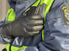 En person i blå uniform med reflexväst och läderhandskar håller en kommunikationsradio vid axeln.