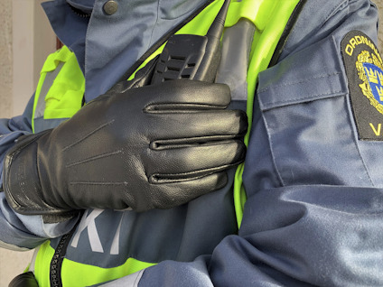 En person i blå uniform med reflexväst och läderhandskar håller en kommunikationsradio vid axeln.