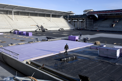 Omkonstruktion av stadion med staplade byggmaterial och arbetare på platsen.