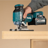 En person använder en Makita-sticksåg för att såga i en träplanka.