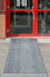 Grå dörrmatta på plattor framför röd glasdörr med öppettider.