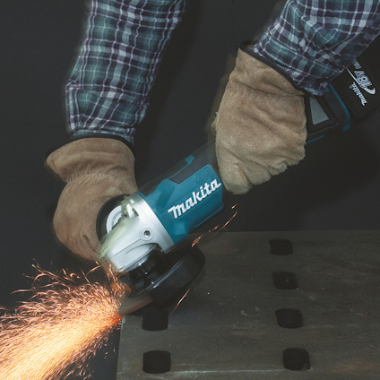 En person använder en vinkelslip med skyddsglasögon och handskar, gnistor flyger från metallplattan.