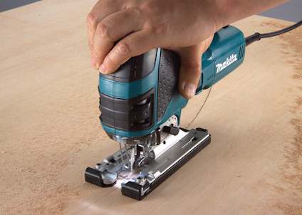 Person använder elektrisk sticksåg för att skära i träskiva.