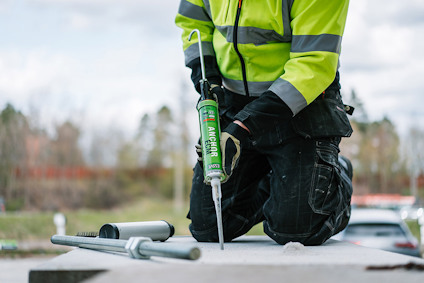 Person i gul skyddsväst applicerar ankarmassa med fogpistol på en byggarbetsplats utomhus.