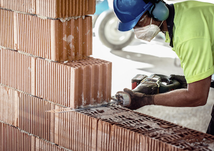 Person i skyddsutrustning skär en staplad mur av tegelstenar med en handhållen såg.