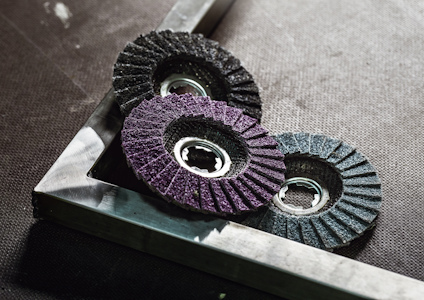 Tre sliphjul i olika färger ligger snett på en metallram på mörk yta.