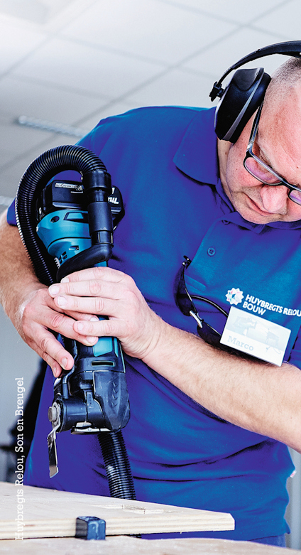 En person med hörselskydd använder en slipmaskin på en träyta.