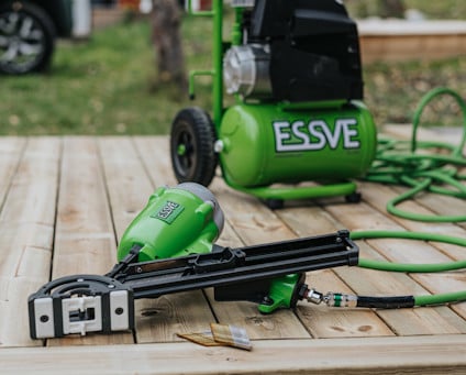 Grön spikpistol och luftkompressor med ESSVE-logotyp, placerade på ett trädäck.