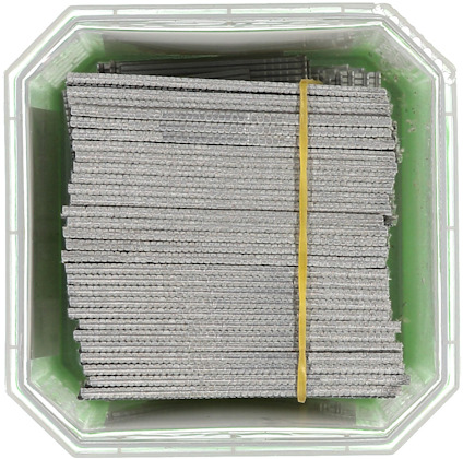 Behållare med staplade grå metallstänger hållna ihop av ett gummiband.