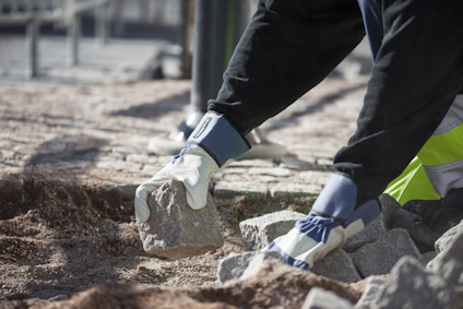 En person med handskar lyfter en sten i en grushög i en utomhusmiljö.