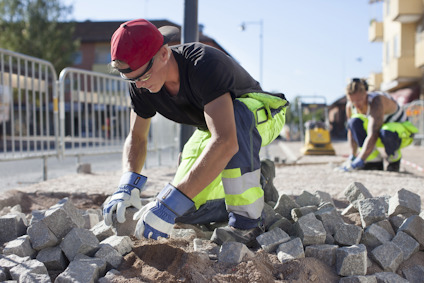 Person i skyddskläder arbetar med stenar på en byggarbetsplats utomhus.
