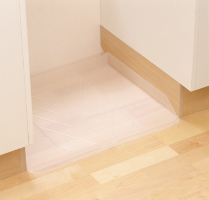 Transparent plastmatta på ljus parkettgolv, placerad i ett kökshörn mellan skåp.