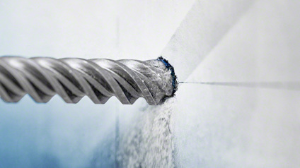 Borrspets borras in i kakelplatta med damm som flyger.