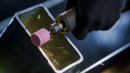 Hand i svart handske slipar en metallkant med ett rosa slipverktyg som skapar gnistor.
