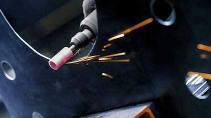 Svetsning med gnistor i mörk omgivning, nära syn på svetsmunstycke och metall.