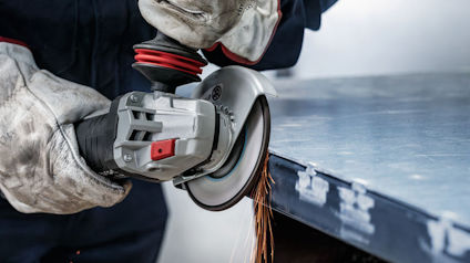 Person med handskar använder vinkelslip på metallstycke.