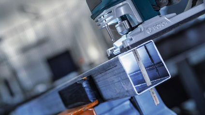 Elektrisk sticksåg sågar genom en metallbalk i en verkstadsmiljö.