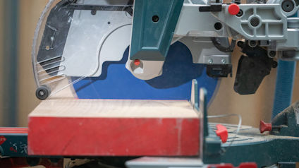 Cirkelsåg som skär genom ett trästycke, röd och silverfärgad ram, blått skydd bakom sågklingan.