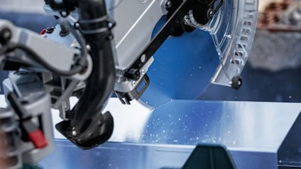 En kap- och gersåg skär genom en metallbit med sågklingan i rörelse, omgiven av arbetsverktyg.