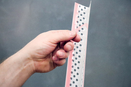 Hand holding en perforerad plastlist mot en grå bakgrund.