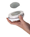 Hand håller vit och silverfärgad rund lampa med magnetisk baksida, avtagbar runt skiva ovanför.