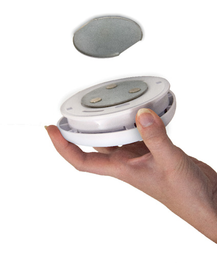 Hand håller vit och silverfärgad rund lampa med magnetisk baksida, avtagbar runt skiva ovanför.